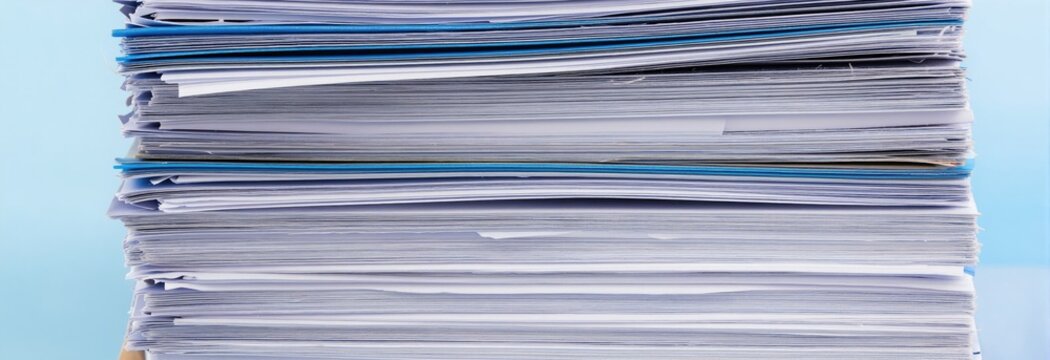 Tall stack of paper documents and blue folders piled high. Office paperwork and files create disorder. Messy, cluttered archive and bureaucracy.