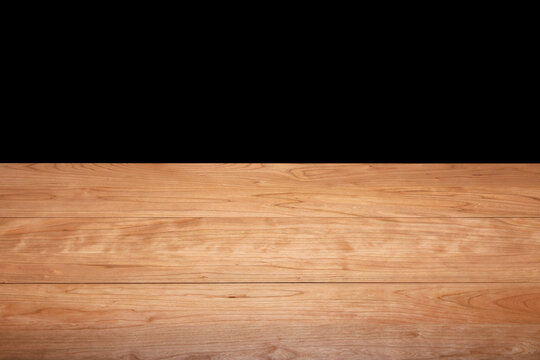 A long, solid cherry wood tabletop against a black background. Wooden tabletop background. Cherry wood grain.