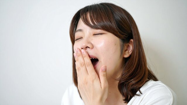 眠そうにあくびをする20代の日本人女性の日常シーン