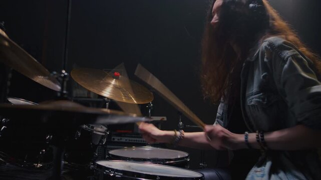 Young female drummer passionately playing a drum kit in a professional rehearsal studio, energetically striking cymbals and drums with drumsticks. Hair flying. Rock Feminist style. Woman power.