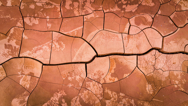 Aerial top down view of cracked dry orange red earth ground texture with deep fissures, drought desertification climate change background, abstract arid soil pattern wallpaper