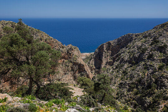 Rugged, steep and rocky cliffs by the Sea of Crete along the Katholiko (or Avlaki) Gorge hike in Crete, Greece, on sunny day, viewed from above.