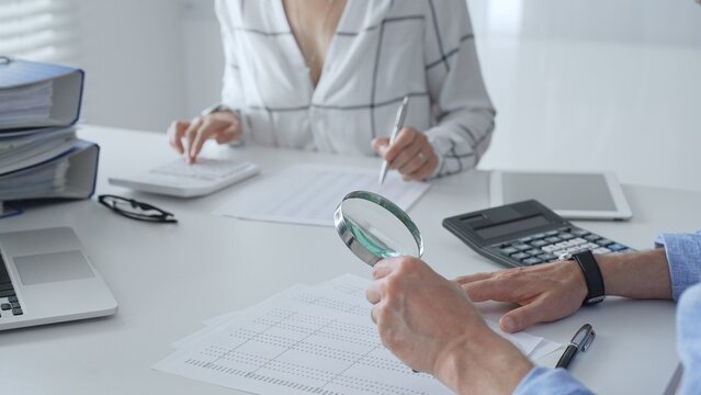 Accounting professionals analyzing financial documents, checking spreadsheet details with calculator and magnifying glass. Audit and taxes in business