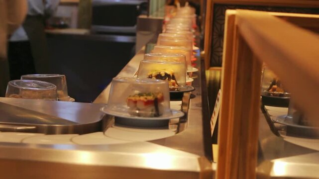 Sushi plates moving on a conveyor belt, close-up Japanese restaurant scene with covered rolls, warm lighting and casual dining