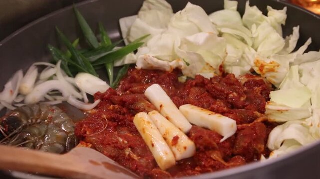 Spicy Korean dak galbi with shrimp, cabbage, rice cakes, and onions cooked in a wok, close-up of Asian restaurant food preparation.