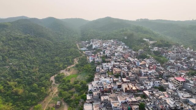 Aerial orbit of dense urban sprawl encroaching on lush green forest ridge. This rotating 360-degree perspective clearly illustrates the environmental conflict of overpopulation and deforestation.