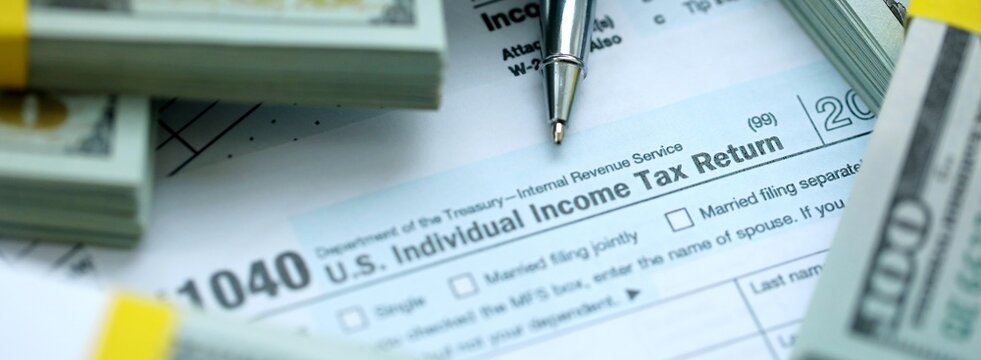 1040 Individual Income tax return form and hundred dollars money bills packs on accountants table