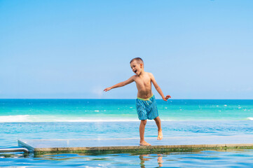 Fototapeta premium happy child playing in infinity pool by tropical ocean