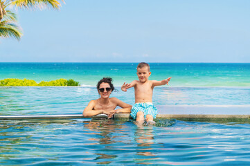 Obraz premium A playful child with his mother in an infinity pool on the shore of the turquoise sea