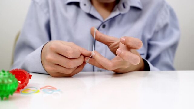 Person adjusts a thin string between fingers. Hands move deliberately, showing focus and control. Small colorful toys sit beside them. Scene implies calm, tactile engagement or therapy