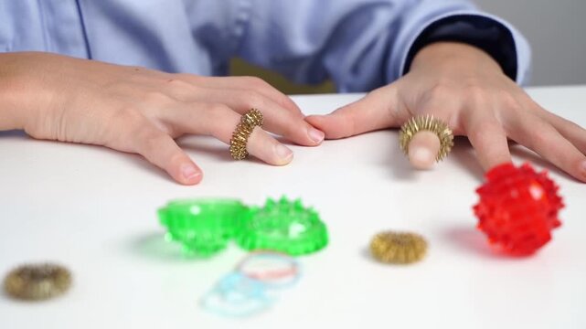 Hands gently manipulate colorful fidget tools. Fingers rest on a clean white surface. Glowing green and red spheres add playful contrast. Calming motion suggests stress relief or sensory engagement