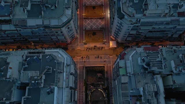 Aerial top-down view over Navarino Square ruins, tilting up to reveal the illuminated historic Rotunda monument in Thessaloniki, Greece at night.
