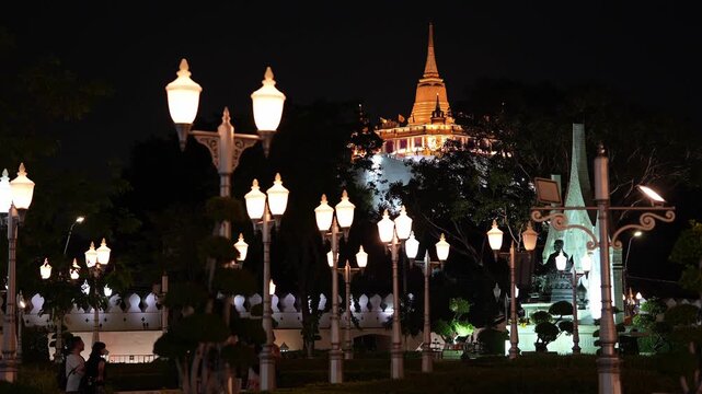 Bangkok, Thailand: Static footage of group of people socializing under city lights of Bangkok, capital city of Thailand with Wat Saket temple on famous Golden Mount illuminated in the background at ni