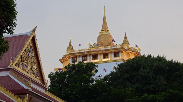 Bangkok, Thailand: Static footage of flags blown by wind in the golden-domed Buddhist stupa of Wat Saket in famous Golden Mount complex of Bangkok, Thailand with the roof of main hall on the side