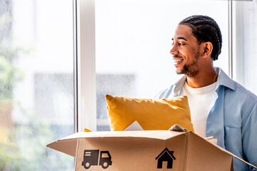 Fototapeta na wymiar young man holding a cardboard box with household belongings, moving into a bright new apartment, concept of home, independence and a new beginning