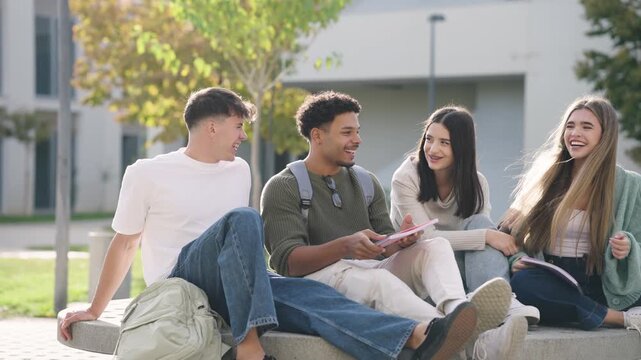 Group of four diverse young students sitting on a bench outdoors. Happy classmates chatting and smiling after lessons on a sunny day