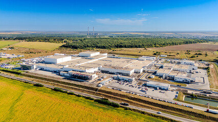 Obraz premium Panoramic aerial view of large industrial plant in rural area. Wide landscape showing a massive manufacturing complex with utility structures and roads under a clear blue sky.