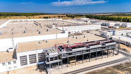 Obraz premium Industrial cooling towers and HVAC systems on factory roof. Detailed view of mechanical cooling equipment and ventilation systems on top of a white industrial building.