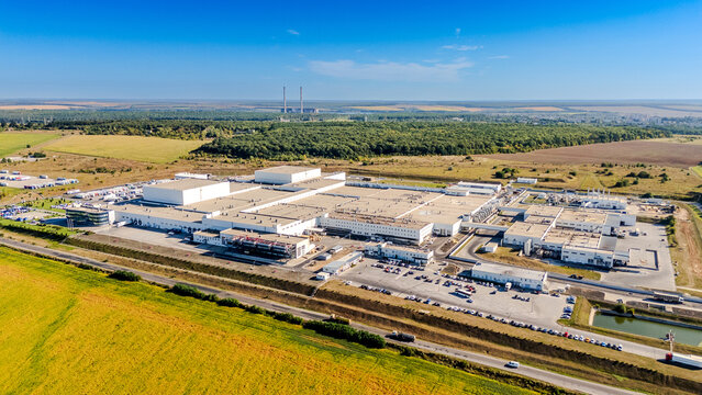 Panoramic aerial view of large industrial plant in rural area. Wide landscape showing a massive manufacturing complex with utility structures and roads under a clear blue sky.