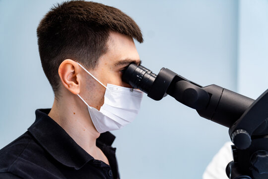 Male stomatologist using high precision microscope for dental surgery. Close profile of a dentist in a surgical mask performing a microscopic endodontic procedure.
