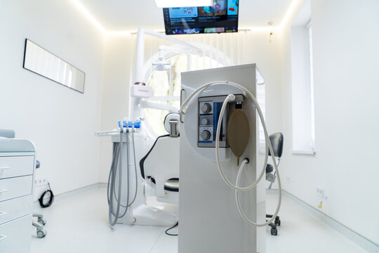 Mobile dental sedation machine with nitrous oxide flowmeter and bag. Modern medical equipment for inhalation anesthesia in a white dental office interior with a patient chair.