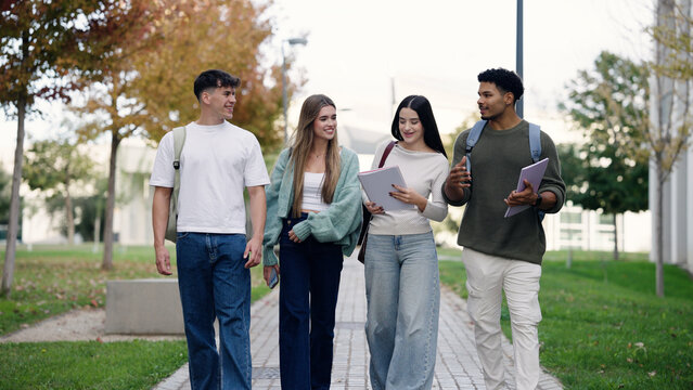 Group of young adult students walking together on a university campus, discussing studies and enjoying friendship outdoors