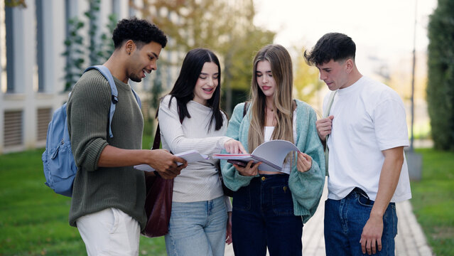 Diverse group of young students discussing and reviewing educational materials together outdoors on a college campus