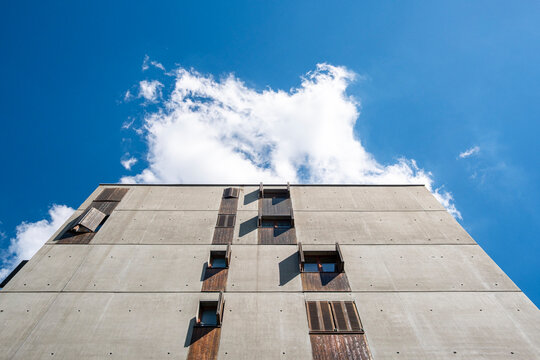 A concrete facade rises in vertical architecture against bright sky and cloud in Lyon, France, with windows cutting an urban geometric surface