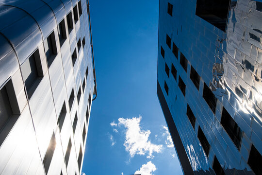 Reflection runs across a glass facade as vertical architecture frames sky and cloud in Lyon, France, creating a sharp urban canyon