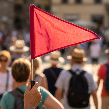 Tour guide holding red triangular flag leading tourist group in sunny city square