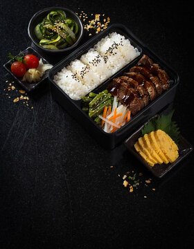 Flat lay view of colorful bento box bento box with rice, vegetables, meat and side dishes arranged in compartments.
