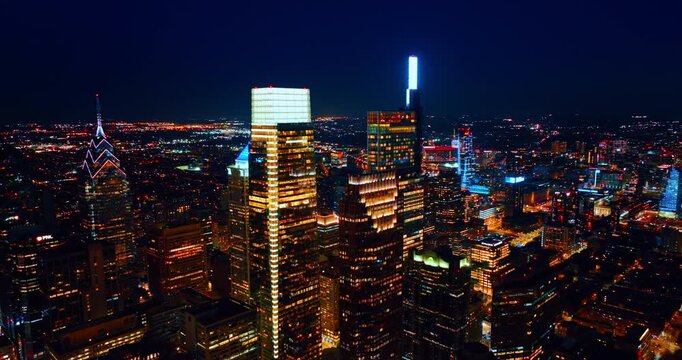 Flight at the tops of skyscrapers illuminated by neon light. Gorgeous architecture of modern Philadelphia, Pennsylvania, USA at night.