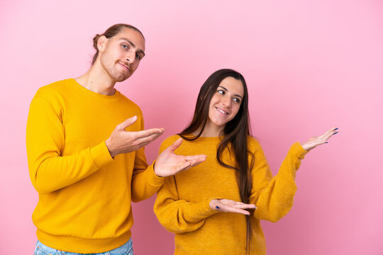 Young caucasian couple isolated on pink background extending hands to the side for inviting to come