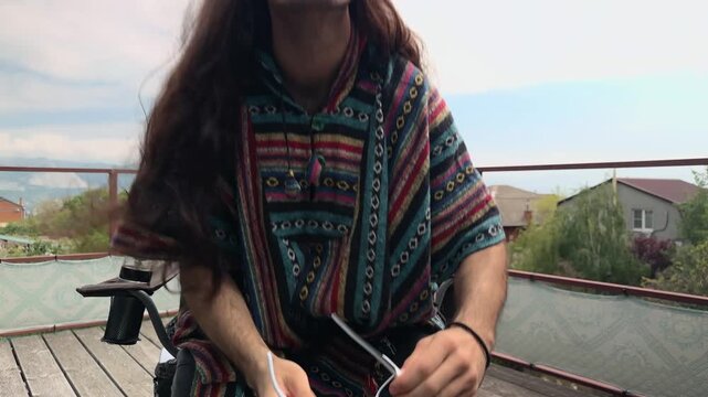 Modern Hippie Man Sitting in Chair on Terrace Wearing Ethnic Poncho and Mirrored Sunglasses Putting Leg over Leg Relaxed Posture with Scenic Mountain View Background Authentic Slow Living Concept