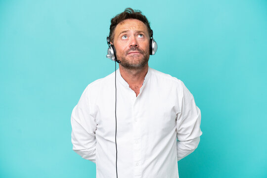 Telemarketer caucasian man working with a headset isolated on blue background and looking up