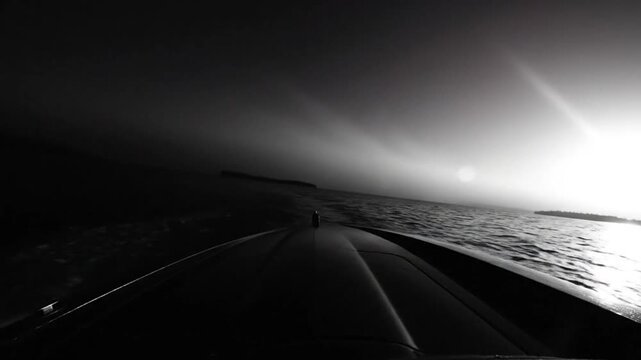 Black and white boat ride across a body of water toward a bright sunny horizon with a view from the bow