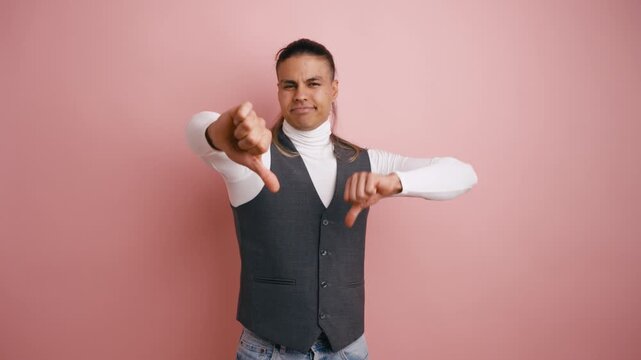 Young latino man with long hair showing a thumbs down gesture. Dissatisfied person expressing his dislike, disapproval, and negation