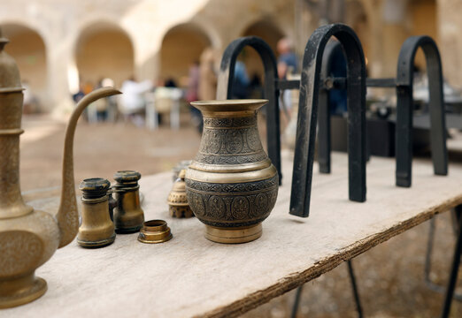 Vintage brass vases and antique binoculars displayed at flea market in courtyard of Franciscan Monastery of Cimiez. Traditional brocante event attracts collectors and tourists to historic site for