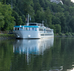 Obraz premium White Passenger Ship Reflected on Calm River Surrounded by Forest