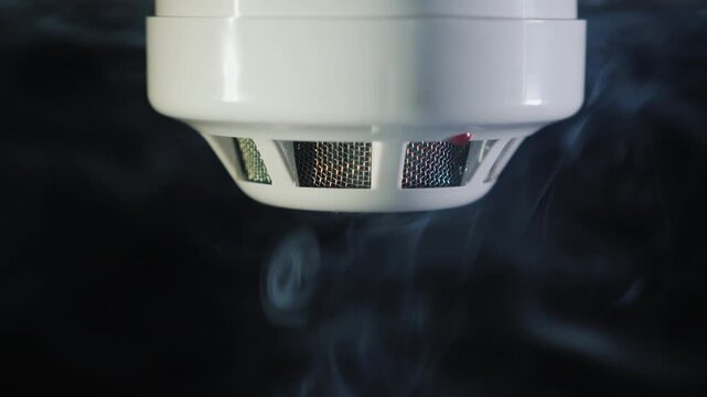 Smoke detector triggered by fire smoke in home environment close up shot.
