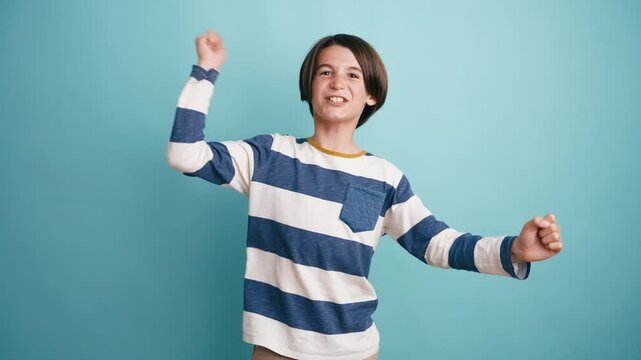 Young boy with short hair in a striped sweater having fun and dancing energetically. Cheerful kid expressing joy and excitement in a studio