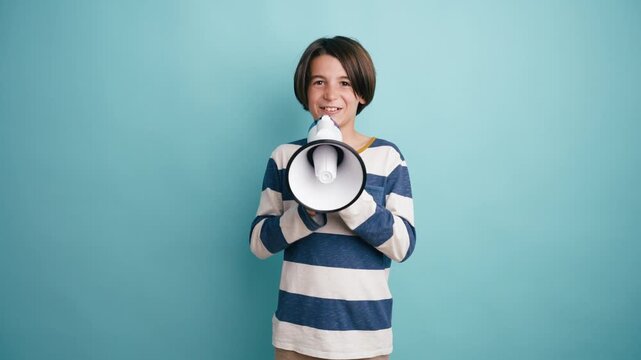 Expressive young boy shouting and speaking into a megaphone. Child making an announcement or protesting against a solid color background