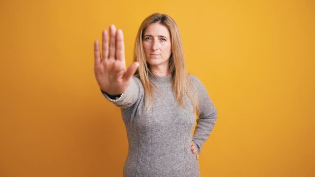 Caucasian woman with a serious face gesturing to stop. Her hand is raised in front of the camera, expressing denial and rejection