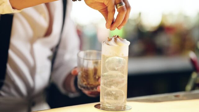 Close up of a skilled mixologist's hands carefully adding the final garnish to a sophisticated alcoholic beverage on a bar counter