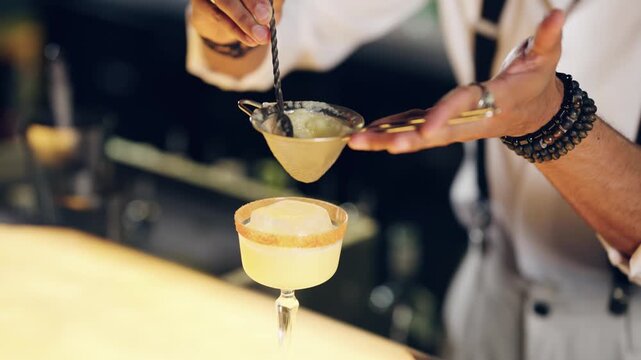Skillful bartender preparing an alcoholic beverage at a bar counter. Professional mixologist mixing and straining a yellow cocktail into a glass