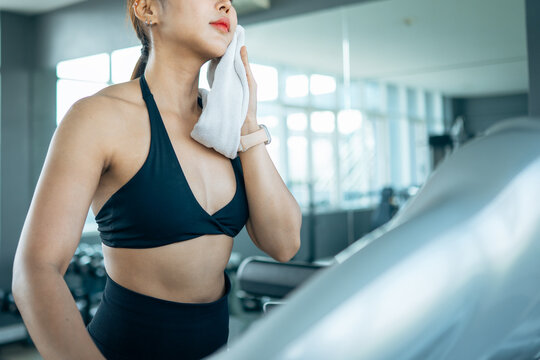 Asian fitness woman wiping sweat with towel after workout in gym. Recovery and cool down concept with hygiene, endurance, healthy lifestyle, post exercise refreshment and active wellness routine.