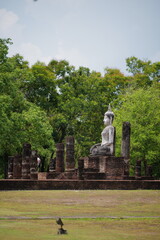 Obraz premium ​Perspective view of the main pagoda and Buddha statue through stone pillars at Wat Mahathat, Sukhothai Historical Park, Thailand.