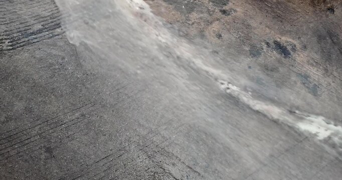 Slow motion close up of water rushing down a sloped asphalt street during intense flooding.
