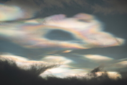 Rare iridescent nacreous cloud glowing in a pastel Arctic twilight sky above dark clouds, soft atmospheric winter scene in Norway