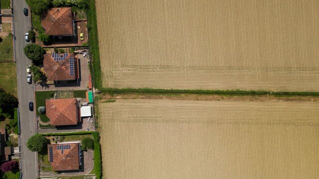 Aerial View of Residential Homes Adjacent to Agricultural Field: An overhead perspective showcases neatly arranged residential houses with manicured lawns bordering a vast, dry agricultural field.